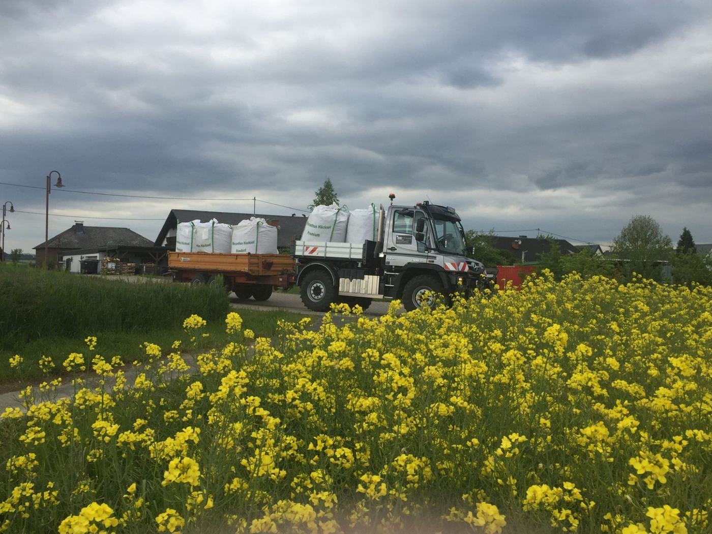 Lkw mit BigBags am Feldrand neben blühendem Raps